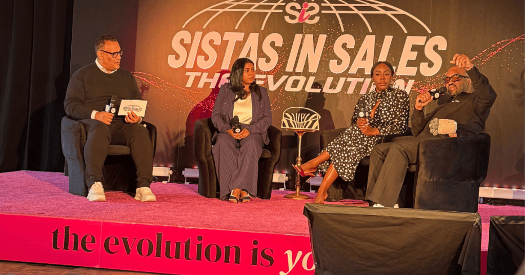 Panel discussion featuring four speakers on stage at the 'Sistas in Sales: The Evolution' event, with a pink backdrop and a modern setting.